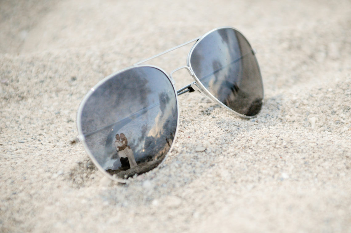 Aviator sunglasses in the sand reflecting bride and groom on Miami Beach