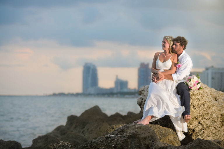 A Miami Beach Wedding Couple Sitting on Rocks Coastal Skyline