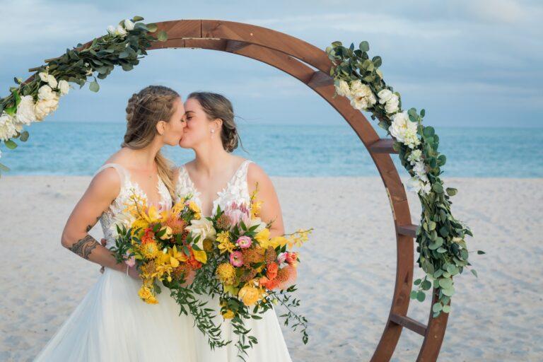 Two brides kiss under a circular wedding arch on a Florida Beach