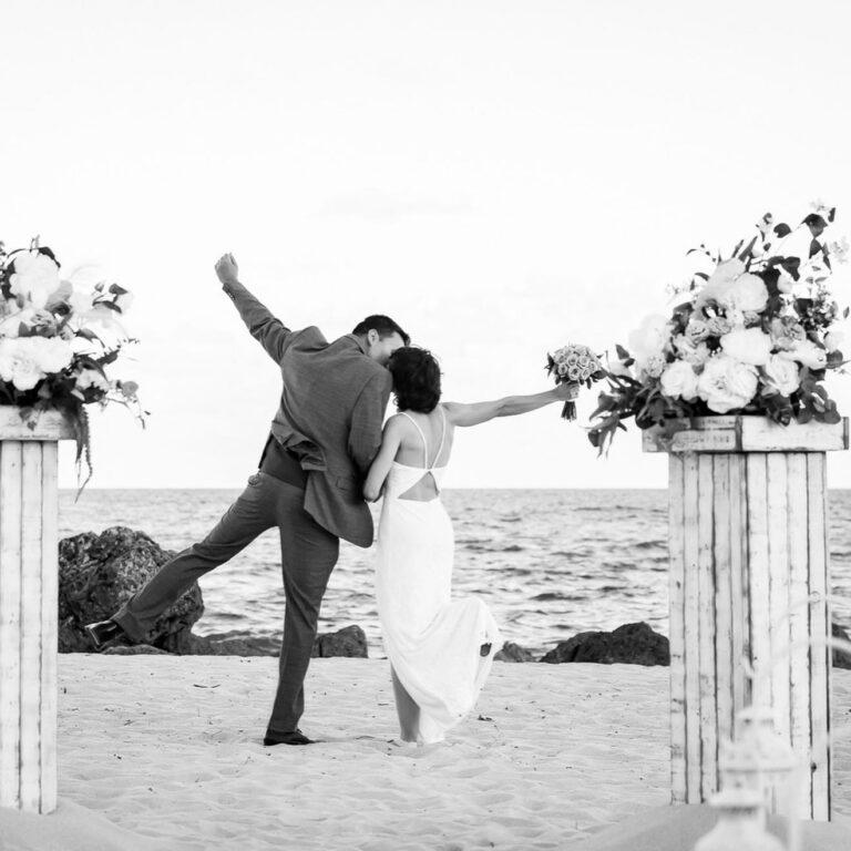 Black & White Photo of Bride and Groom Jumping for Joy at their beach wedding