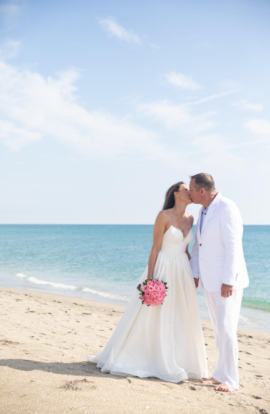 Bride and Groom embrace on Hutchinson Island Beach, Floria. Bride holds pink bouquet of roses.