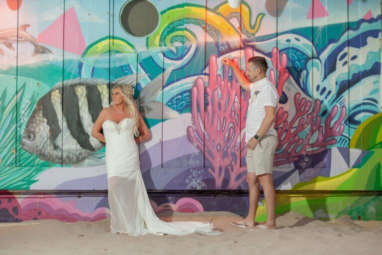 Bride and groom stand behind a colorful mural - Lauderdale-by-the-Sea